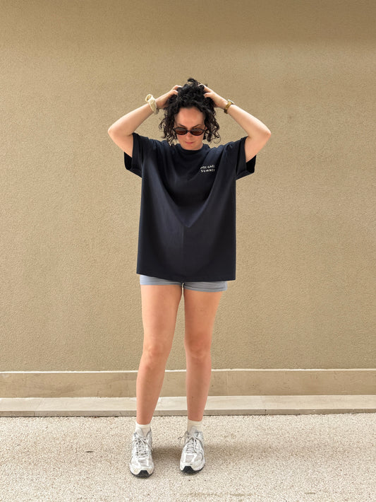 Person wearing a navy oversized Hot Gael Summer t-shirt and shorts against a beige wall.