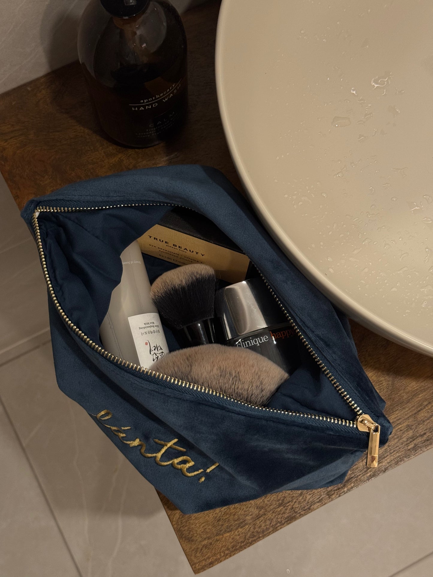 Open navy blue makeup bag with cosmetic items on a wooden surface