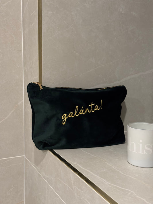 Emerald pouch with 'galánta' embroidery on a tiled bathroom shelf.