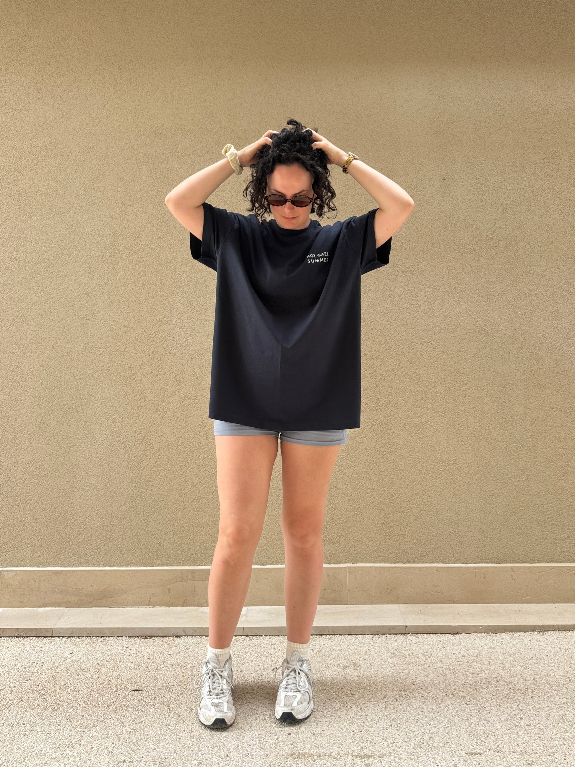 Person wearing a navy oversized Hot Gael Summer t-shirt and shorts against a beige wall.