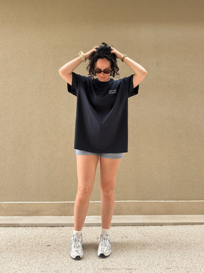 Person wearing a navy oversized Hot Gael Summer t-shirt and shorts against a beige wall.
