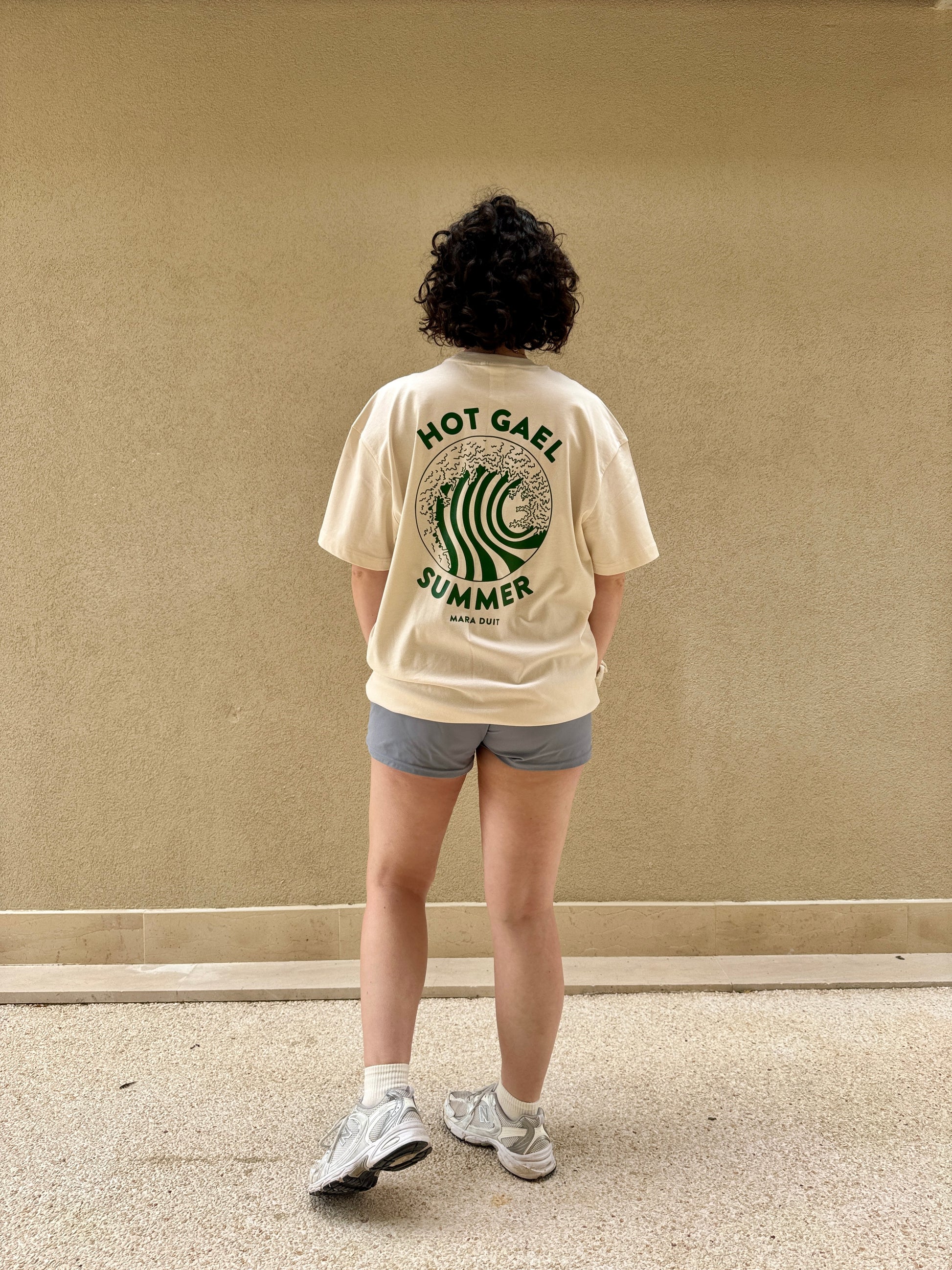 Person wearing a cream t-shirt with hot gael summer text and graphics, standing against a plain wall.