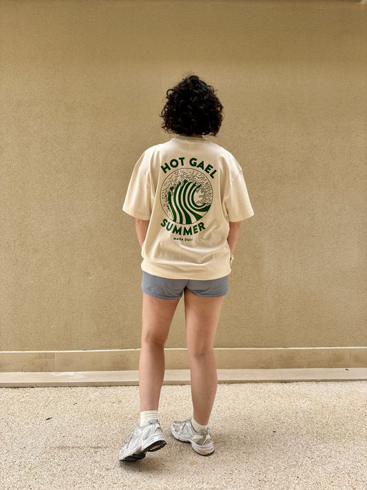 Person wearing a cream t-shirt with hot gael summer text and graphics, standing against a plain wall.