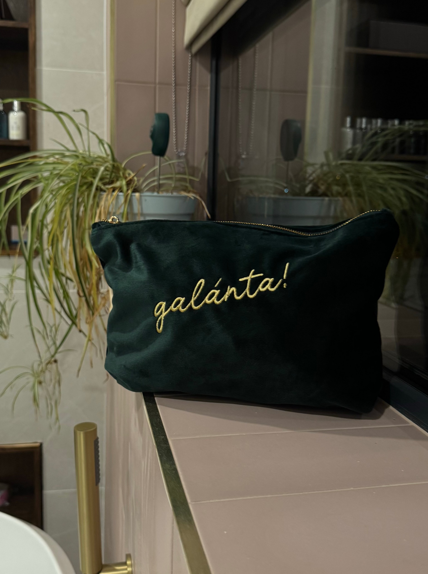 Dark green pouch with 'galanta!' text on a counter in a bathroom setting